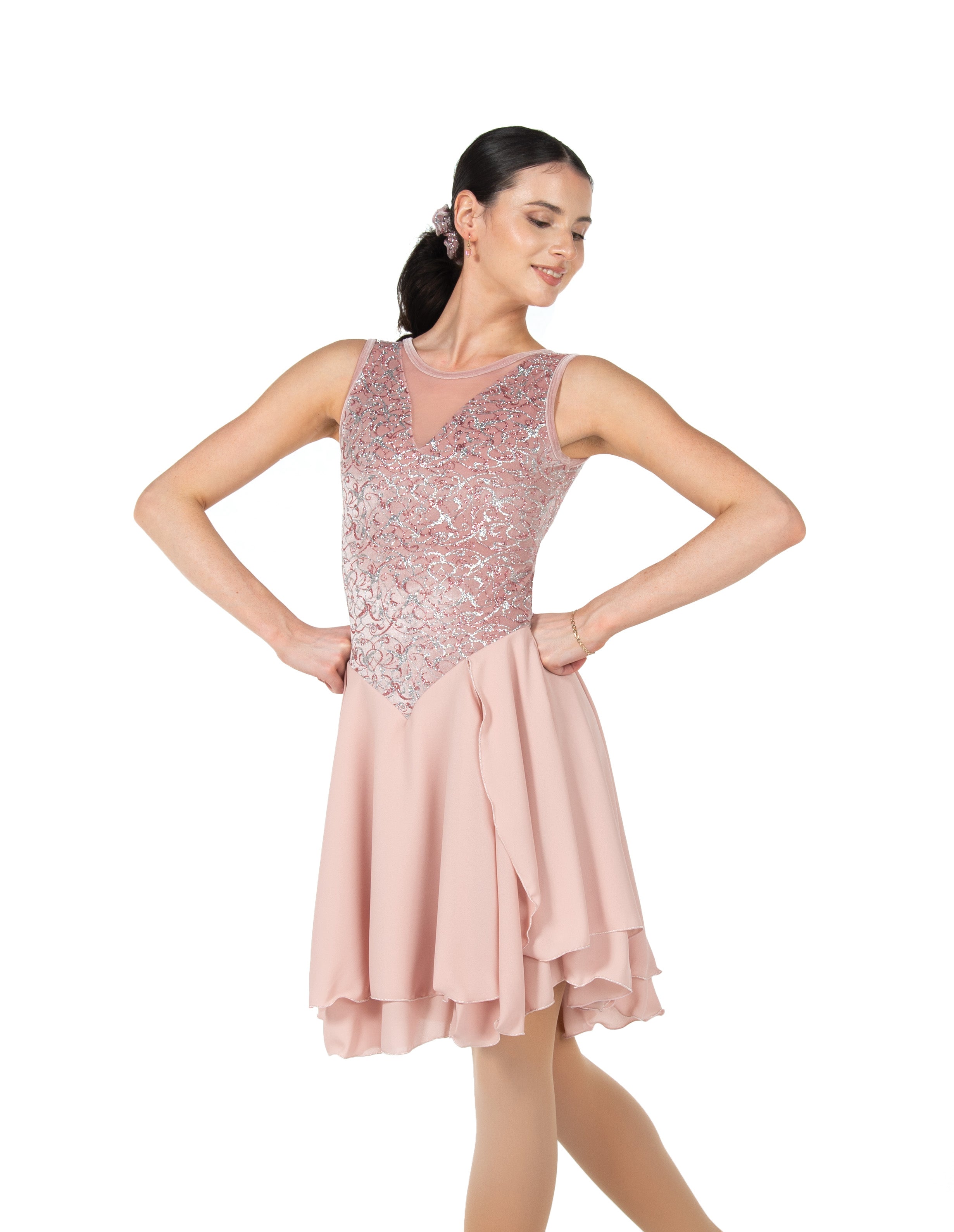 Model posing in JR205 blush skating dress featuring a sparkling velvet bodice and flowing georgette skirt. Designed for elegance and movement.