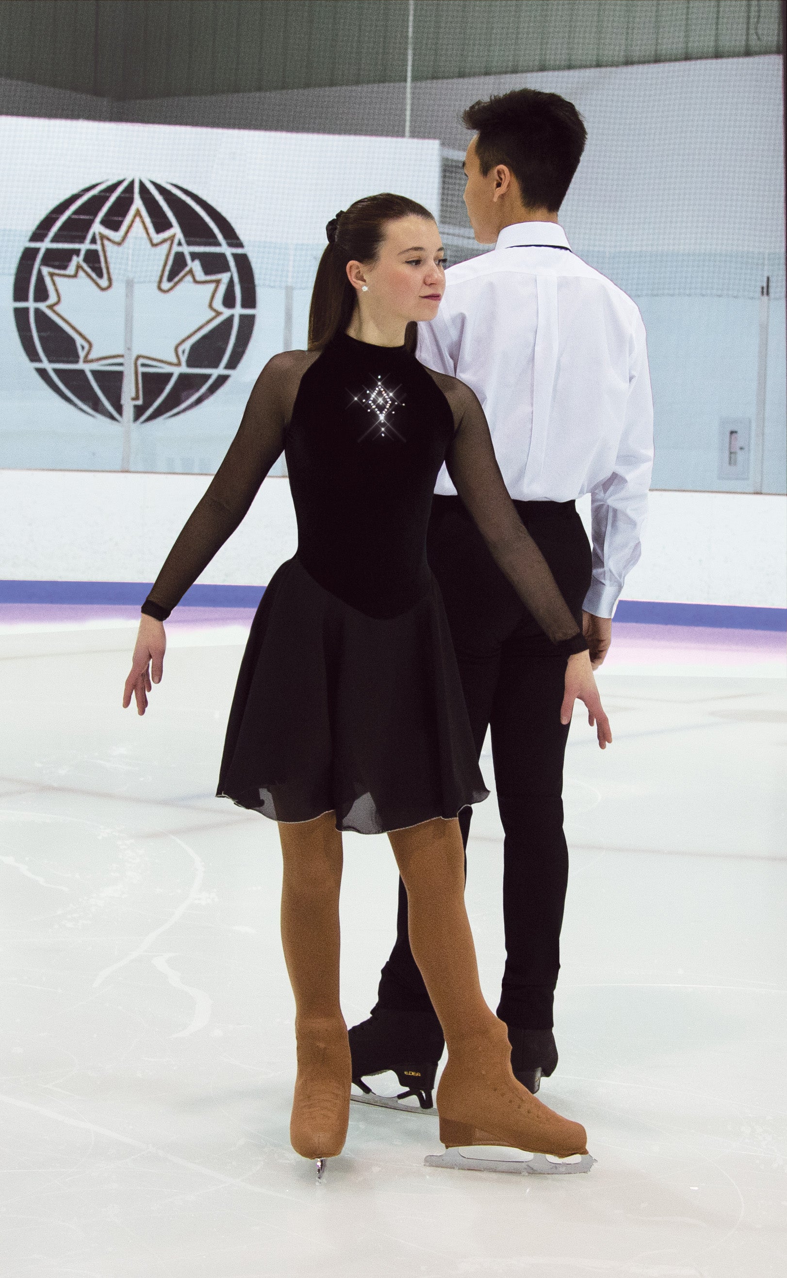 JR98 Coronet black skate dress worn during a pair skating routine. Features mesh sleeves, crystal detail, and flowing skirt.