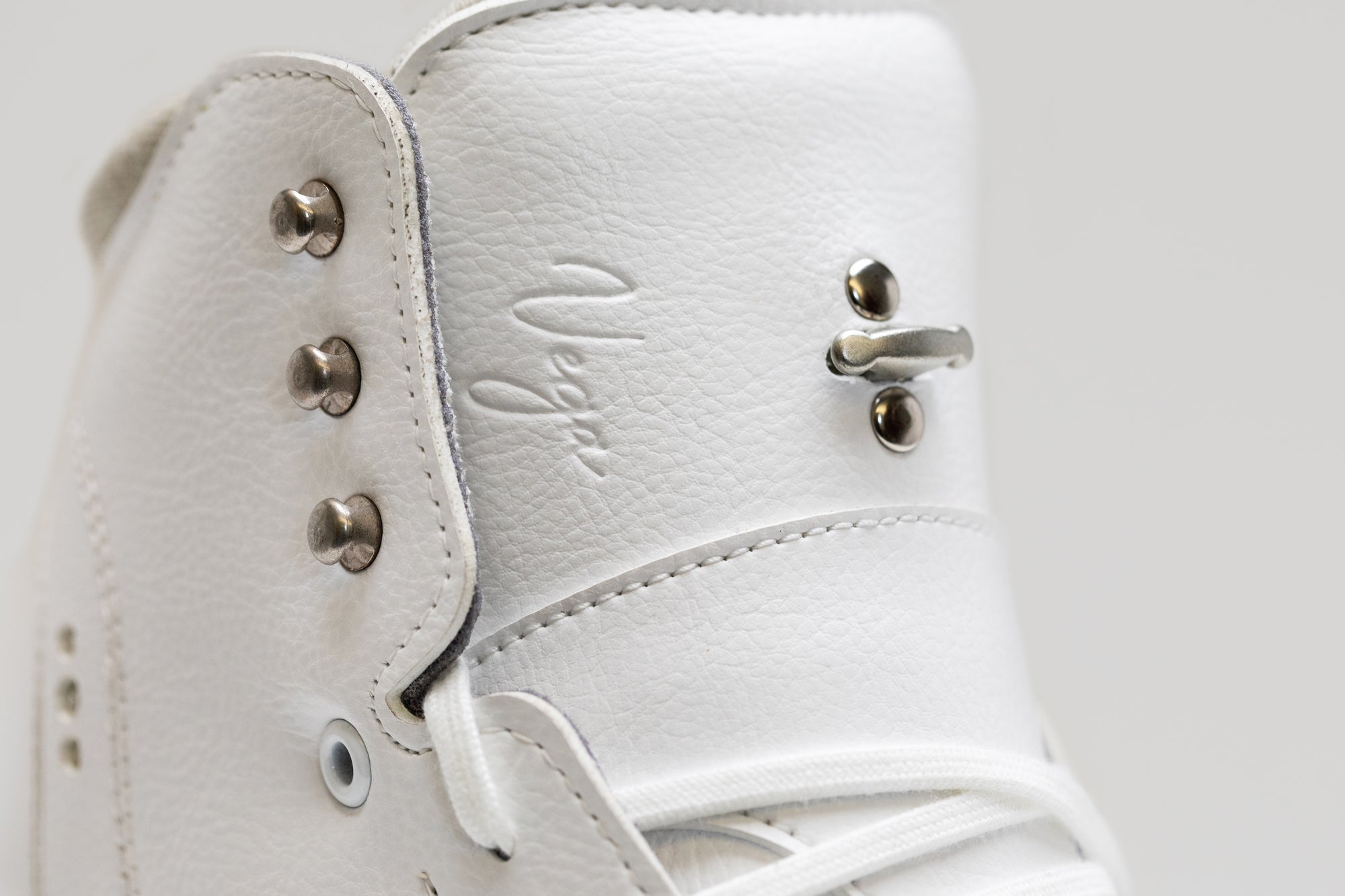 Close-up of Riedell Vega womens figure skate boot tongue showing embossed Vega logo and secure lacing hook for enhanced ankle support.