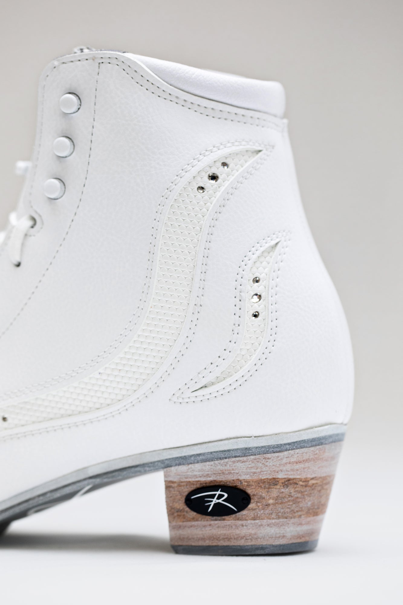Detailed heel view of Riedell Elara womens figure skate boots highlighting stitched accents and Riedell logo on wooden heel.